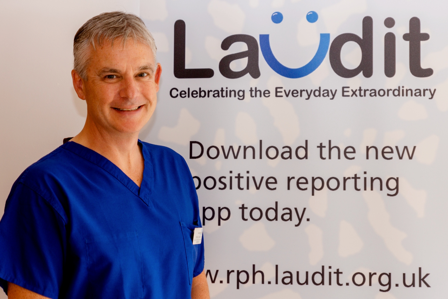 Will wearing blue scrubs, smiling in front of a banner saying Laudit - Celebrating the everday extraordinary
