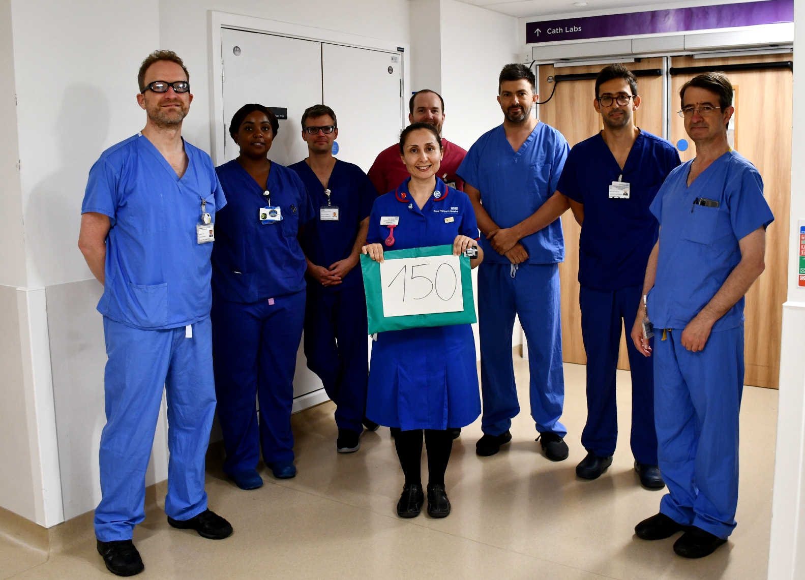 Eight people standing in scrubs and blue nursing uniforms.