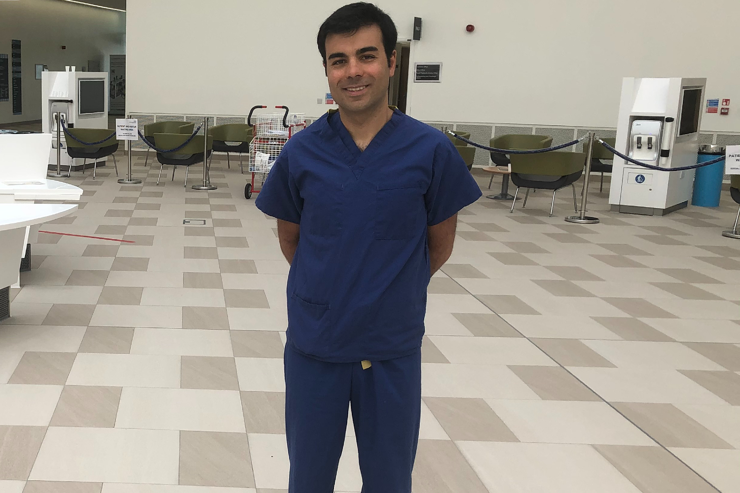 A man standing, wearing blue hospital scrubs.