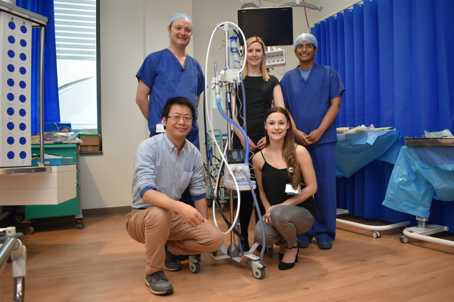 Five people in a hospital room standing around medical equipment.