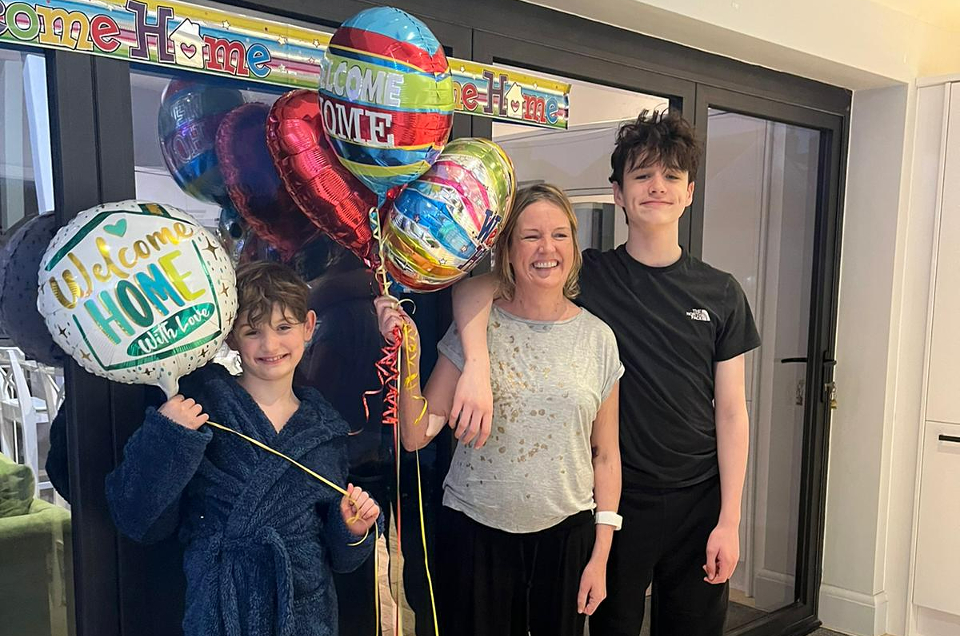 Nicola hugging her two sons, surrounded by 'welcome home' banners and balloons.