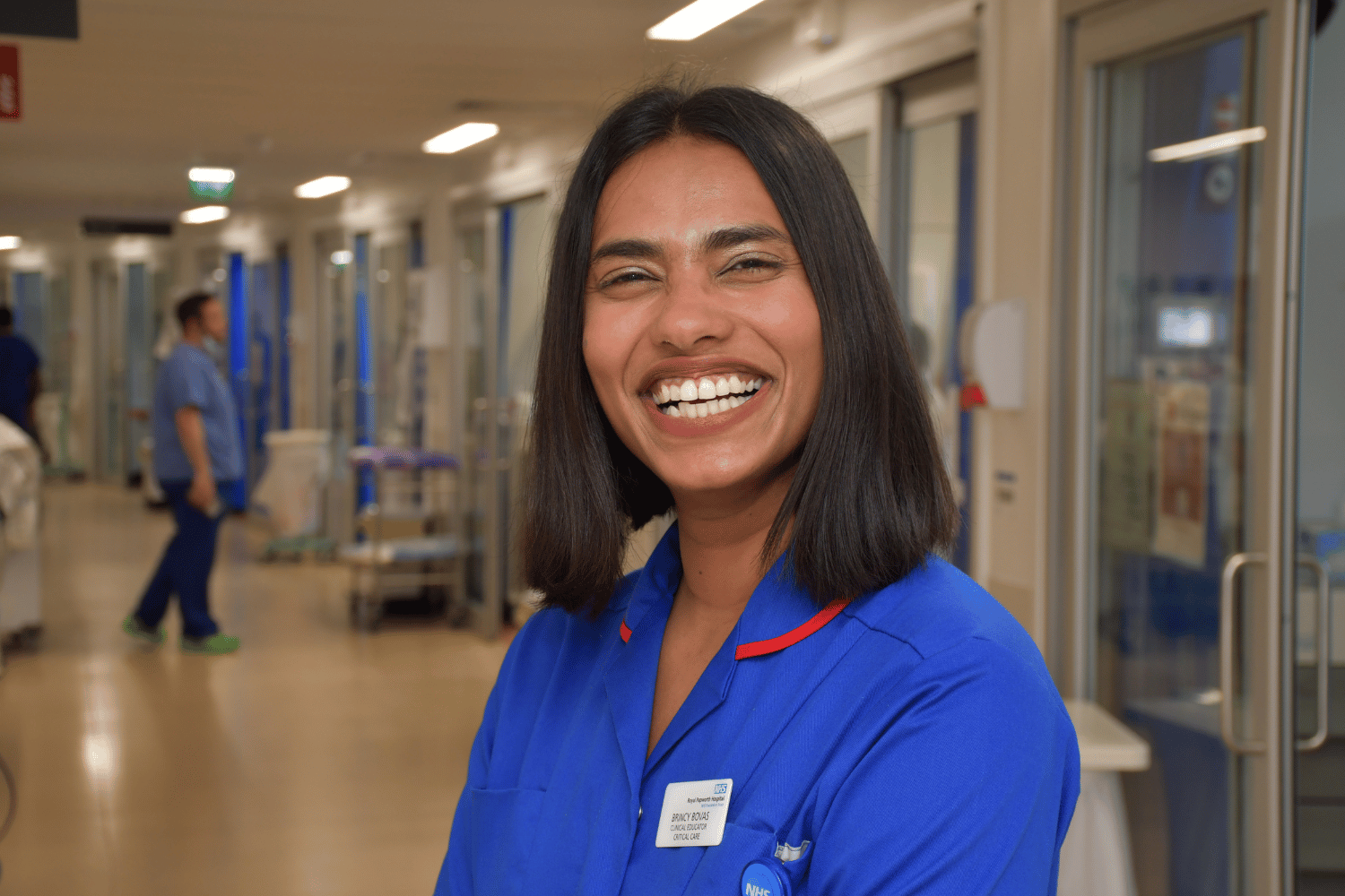 Brincy wearing a blue nurses uniform, smiling in a hospital corridor.