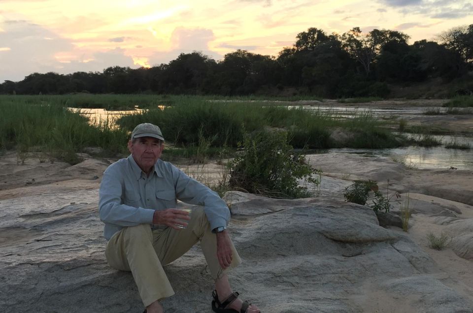Sir Terence on safari in South Africa, sitting down on rocks with a glass of water in his hand.jpg