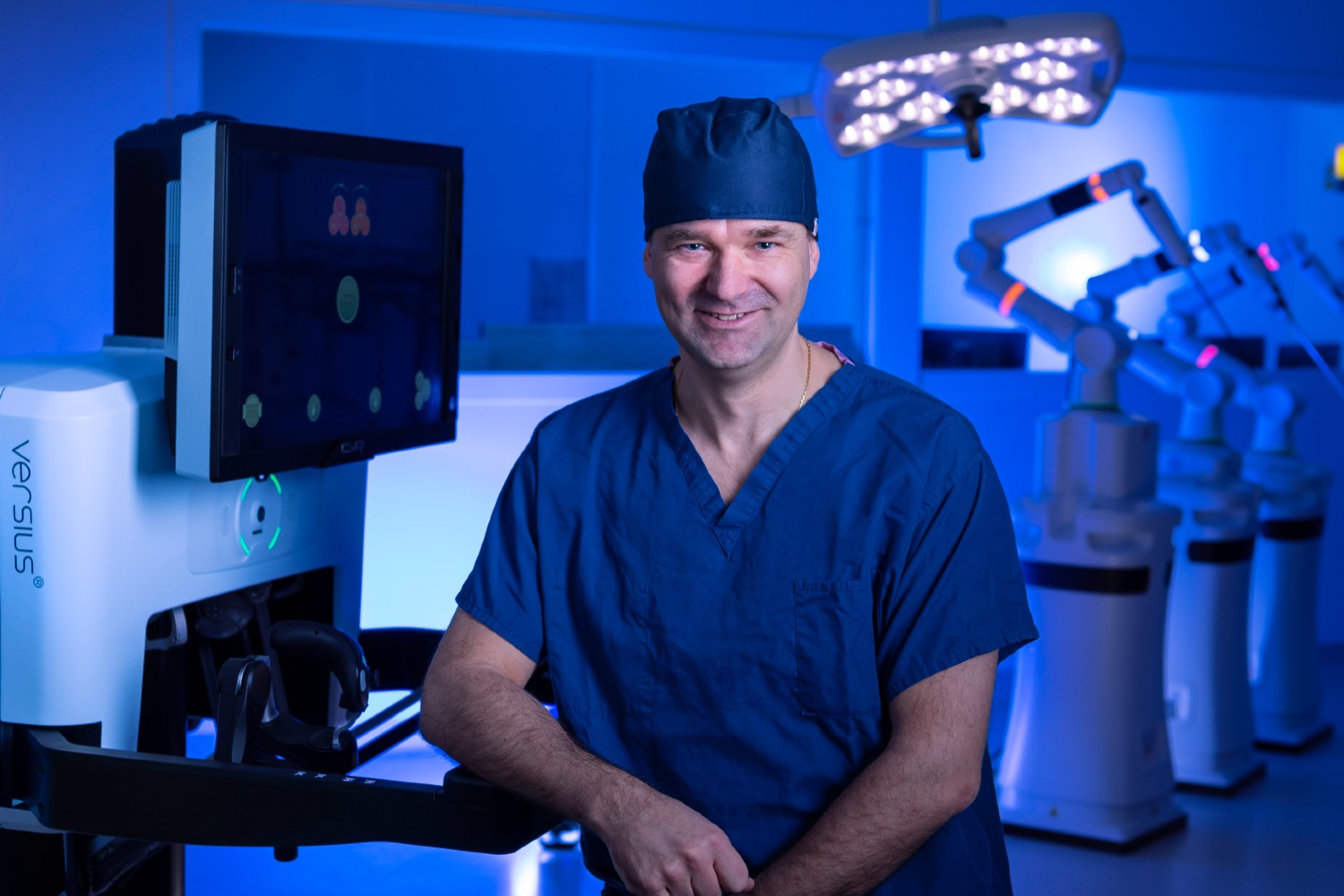 A person in a blue surgical gown and theatre hat stands next to the new surgical robot.