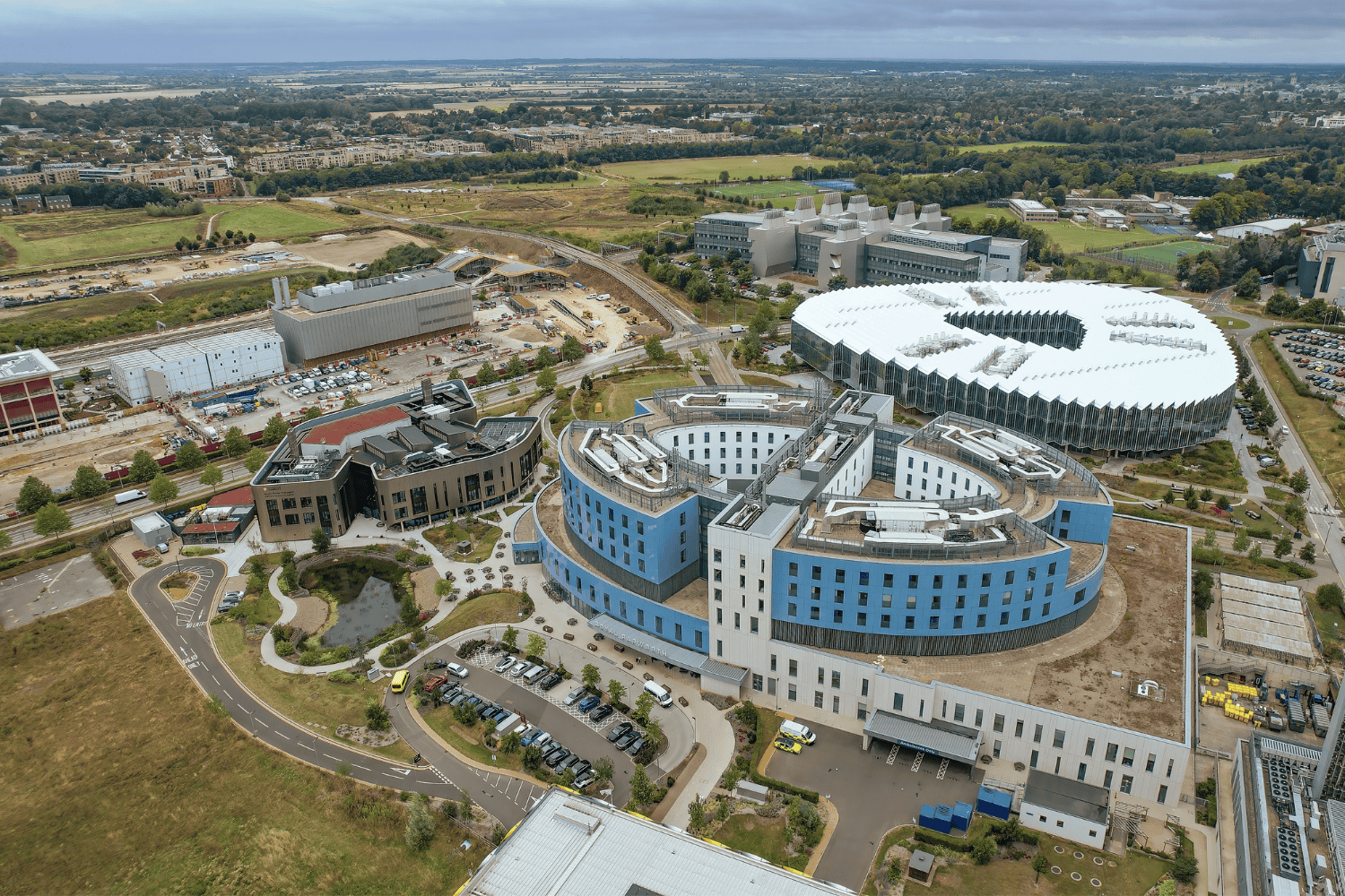 An aerial photo of a blue, curved building with houses and fields in the background