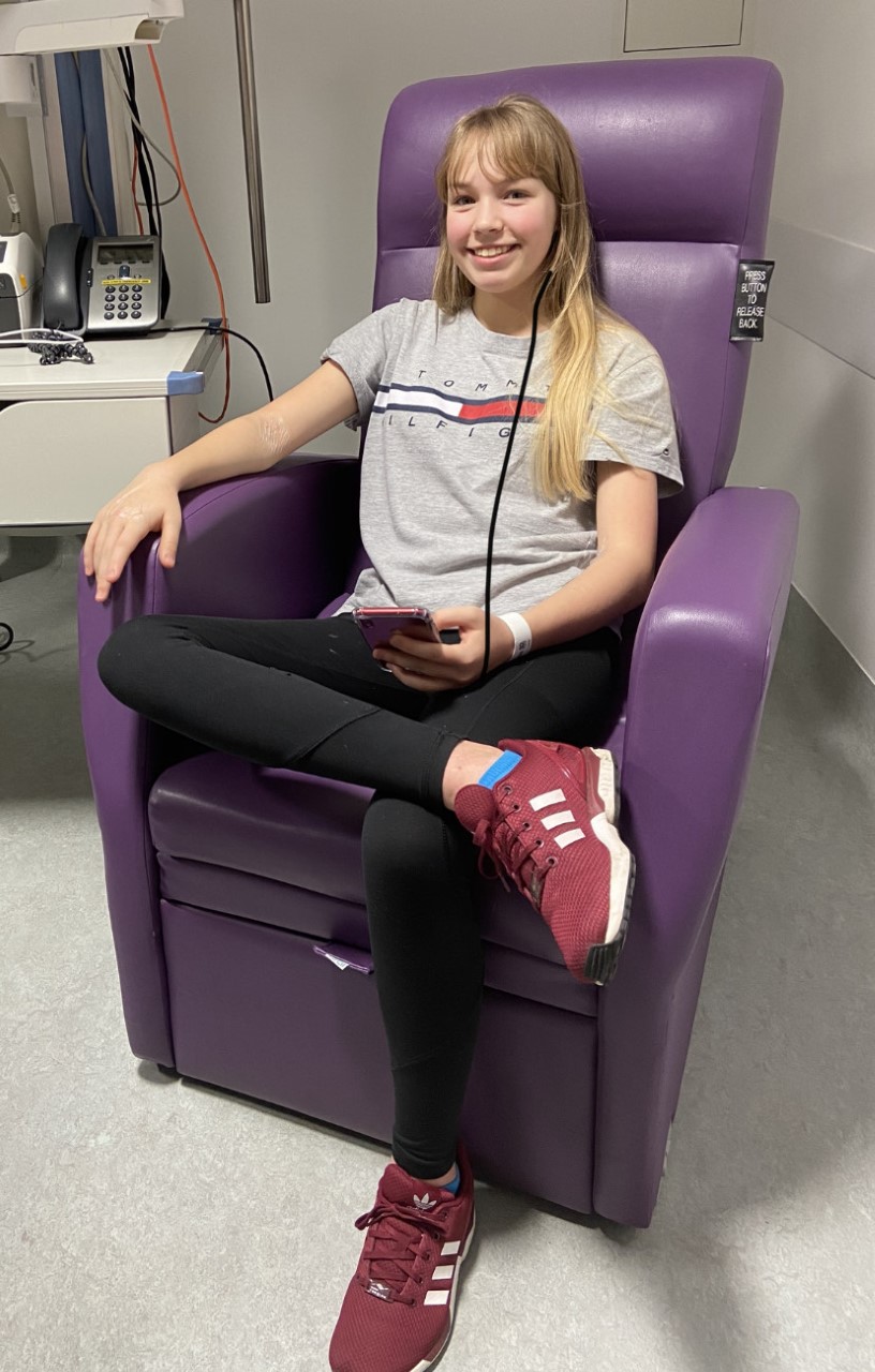A girl smiles while listening to music and sitting in a purple chair.