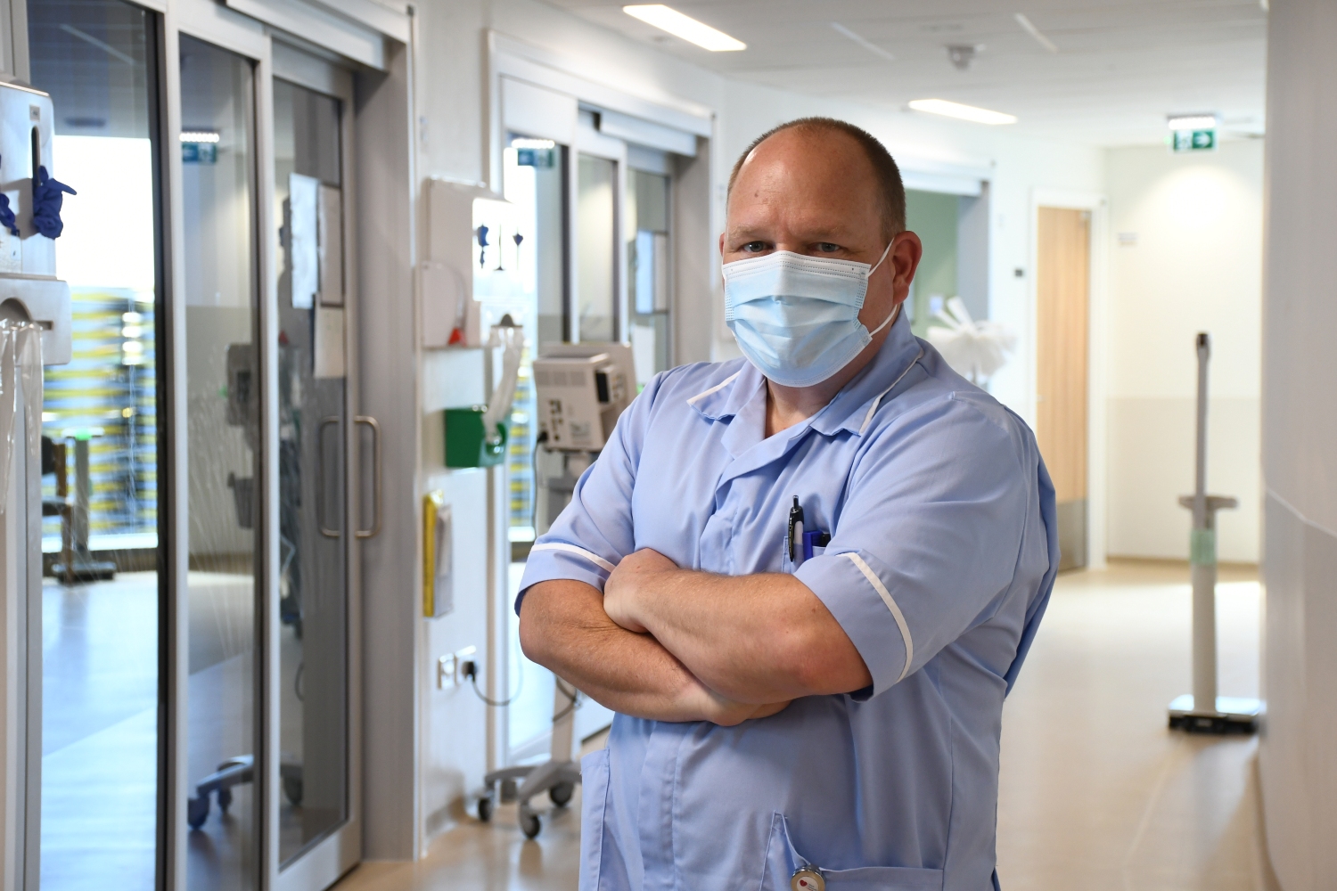 Robin in a pale blue uniform standing in a hospital ward corridor.