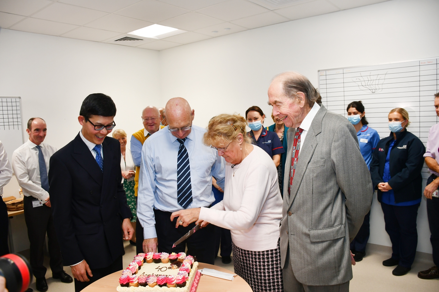 Sandy cuts a cake with several other people standing nearby.