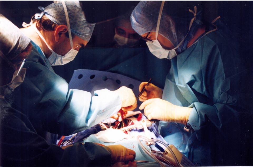 Sir Terence English operating, wearing a blue hat and white mask, with a light shining on his white gloves