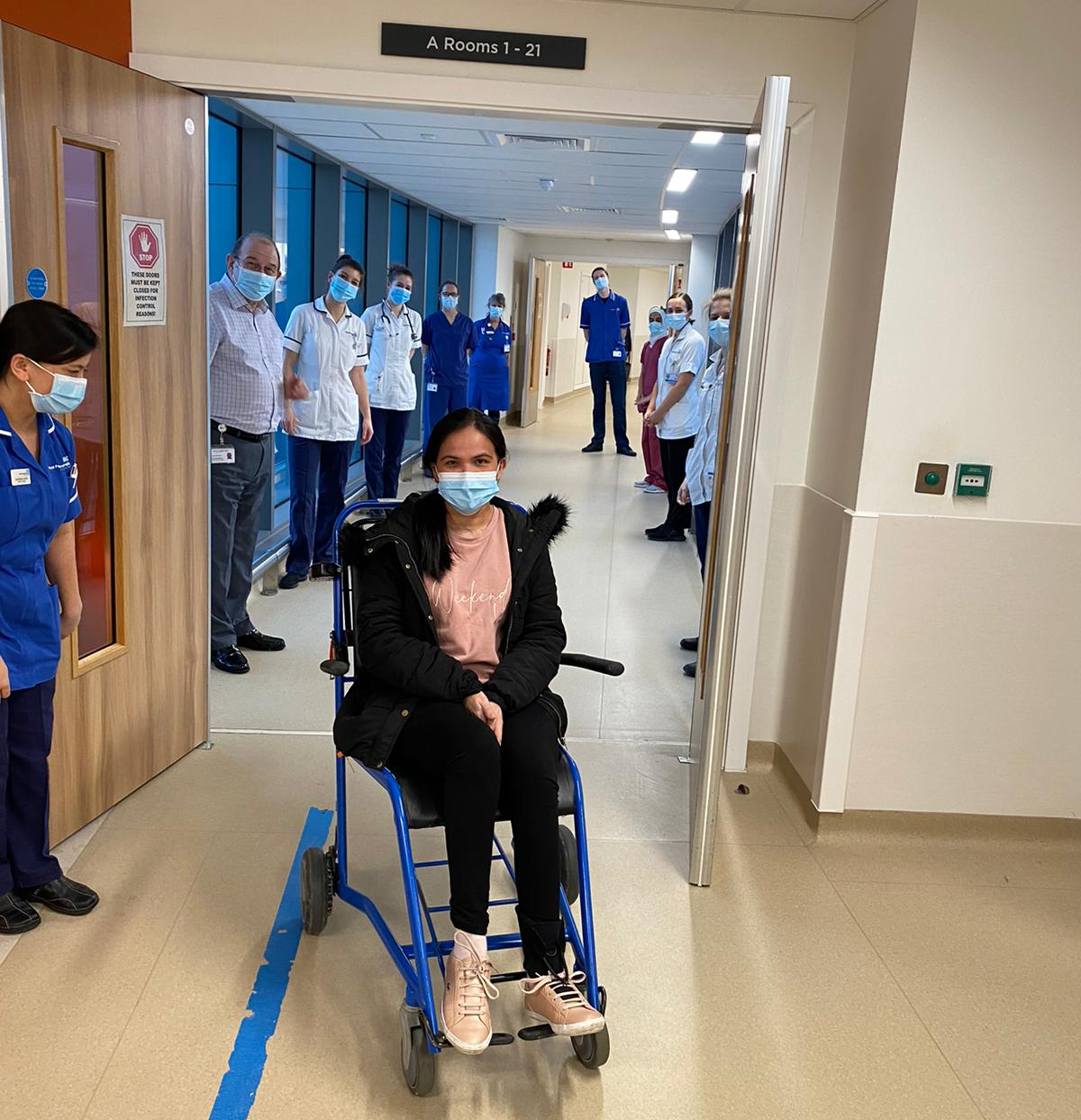 A woman in a wheelchair with NHS staff lining a corridor behind.