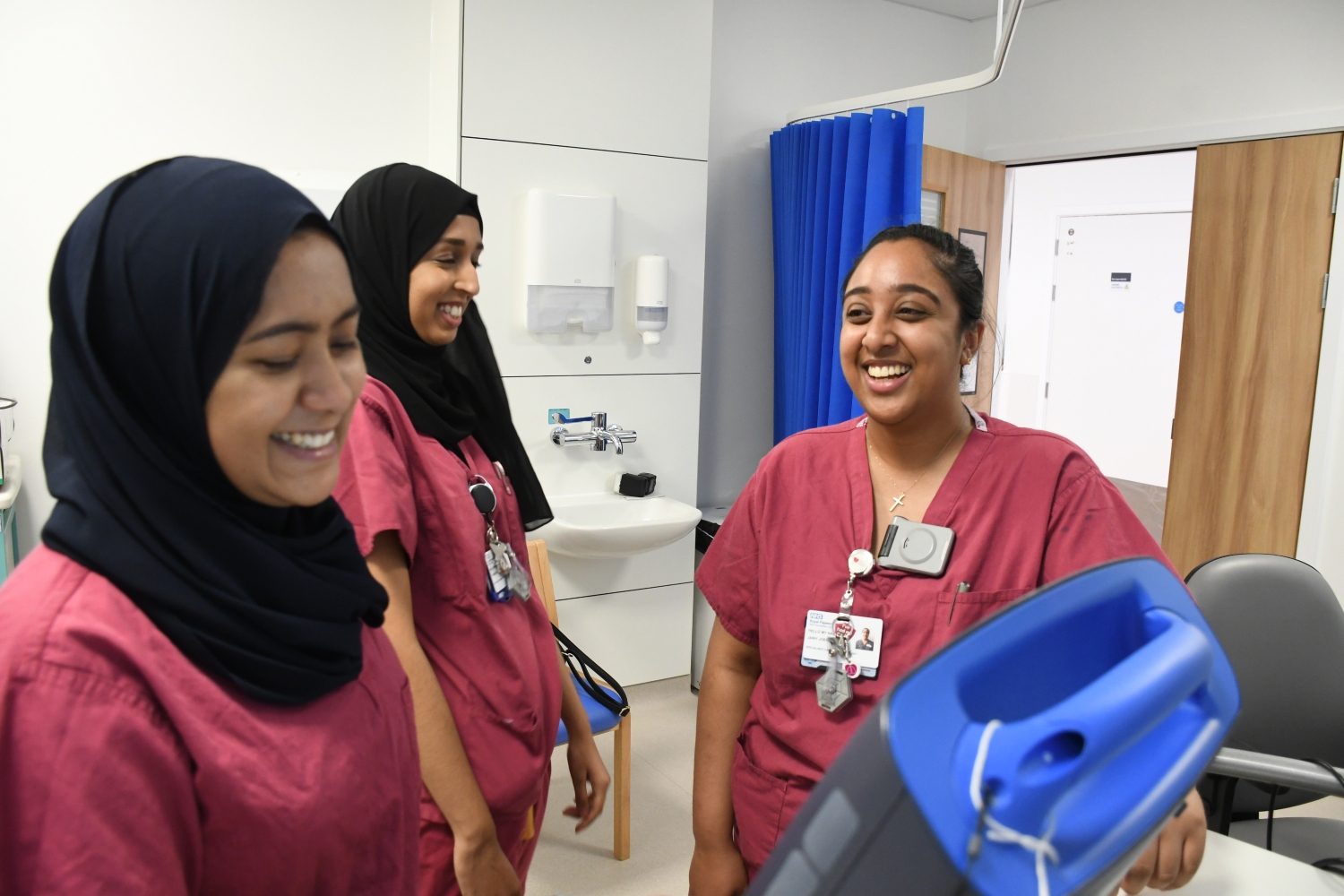 Three people in raspberry coloured scrubs laughing and smiling