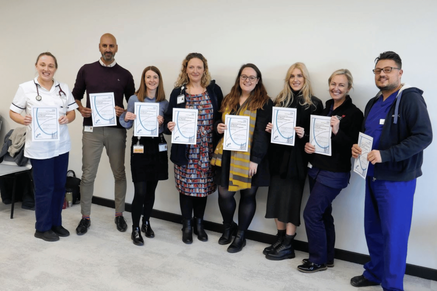 Eight people standing in a line holding certificates in front of them.