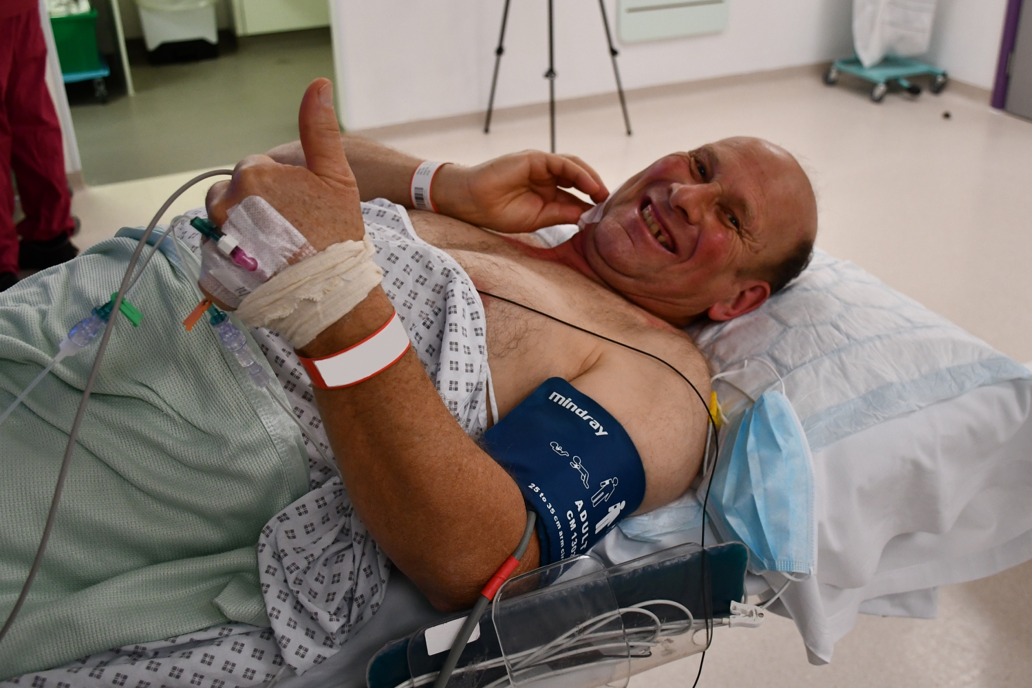 A person on a hospital bed gives a thumbs up.
