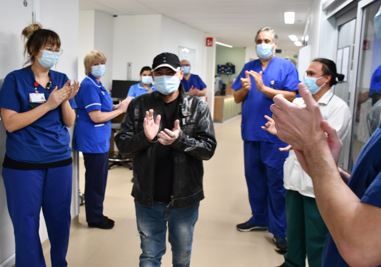 A man walking down a corridor clapping while nurses and medical staff on either side of the corridor also clap.