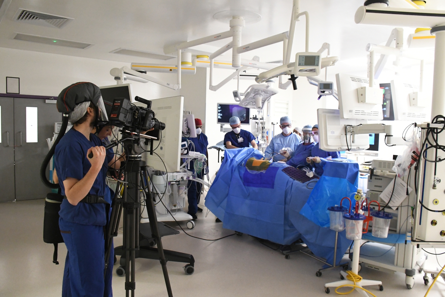 Two people with cameras and film kit stand in an operating theatre during surgery.