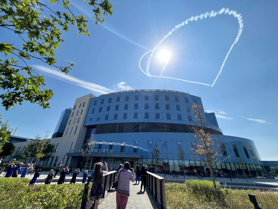 People stood outside a building. A white heart is drawn in the blue sky above.