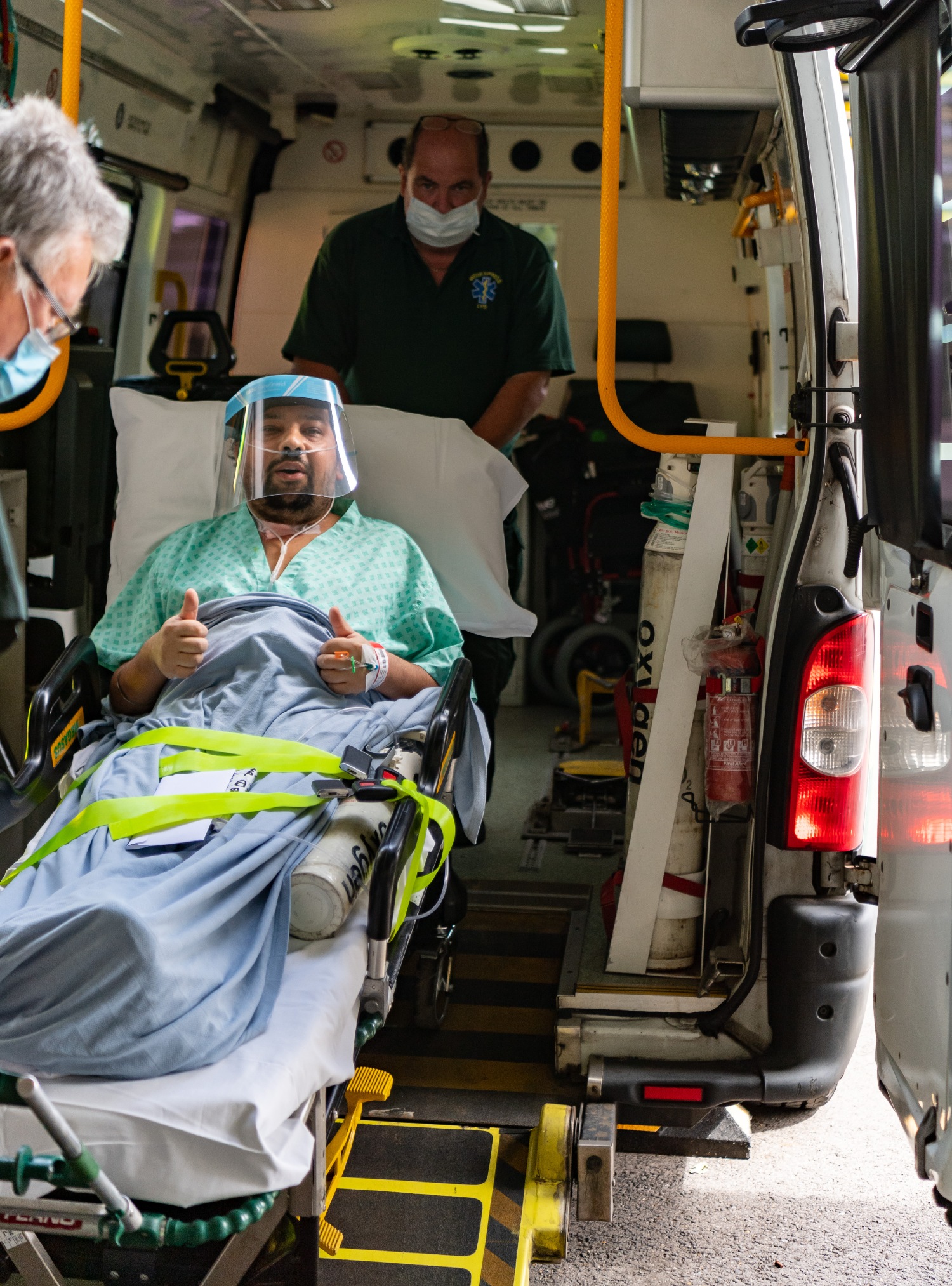 A patient in a bed is wheeled into the back of an ambulance by staff in green uniforms. 