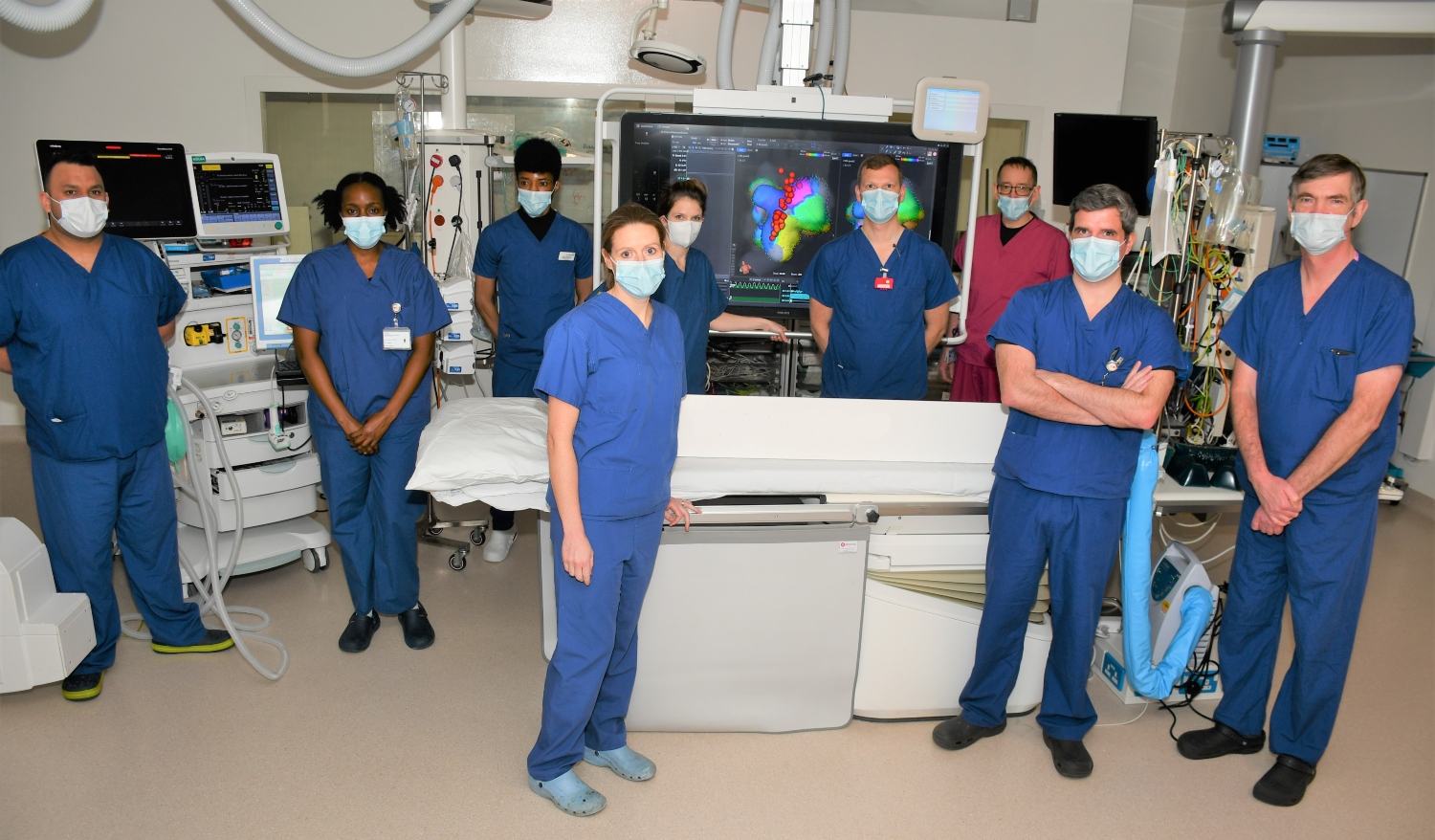 Nine people standing in blue scrubs in a hospital operating room.