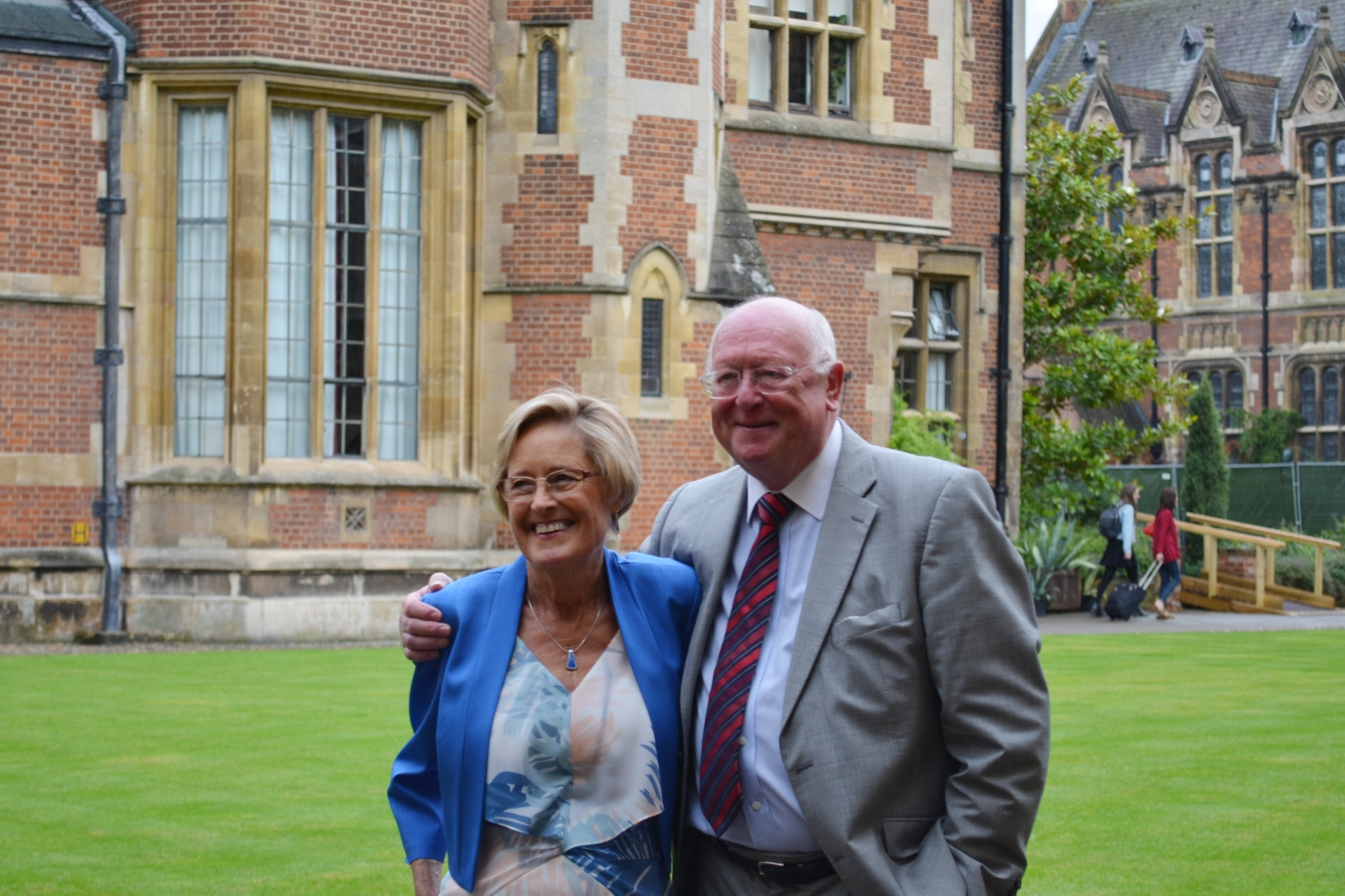 Carol Town in a white and blue dress and blue blazer hugging John Wallwork in a suit, outside.