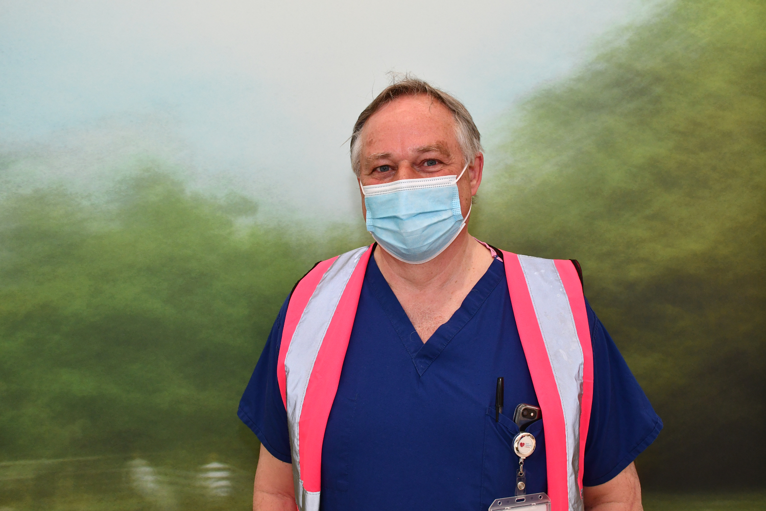 A person wearing a mask and blue scrubs with a pink high-vis vest.