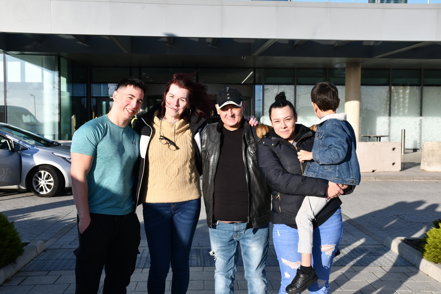 Four people and a child standing outside a hospital, smiling.